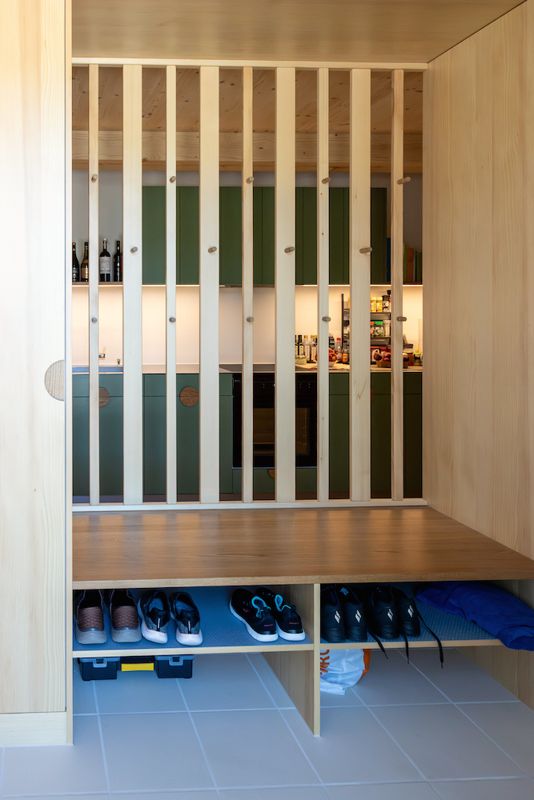 Garderobe mit Sitzbank hinter einem Raumteiler aus Holzlamellen
